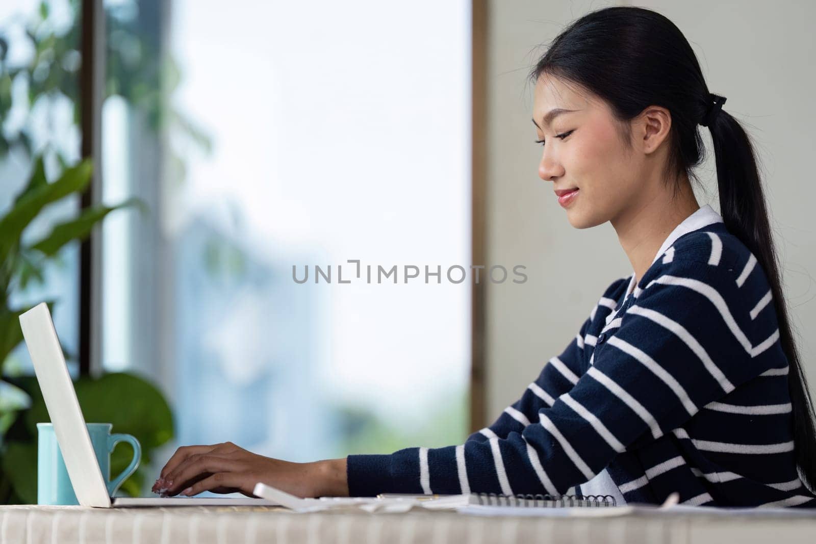 A young woman works on her laptop while managing her finances and bills at home, illustrating modern financial management.