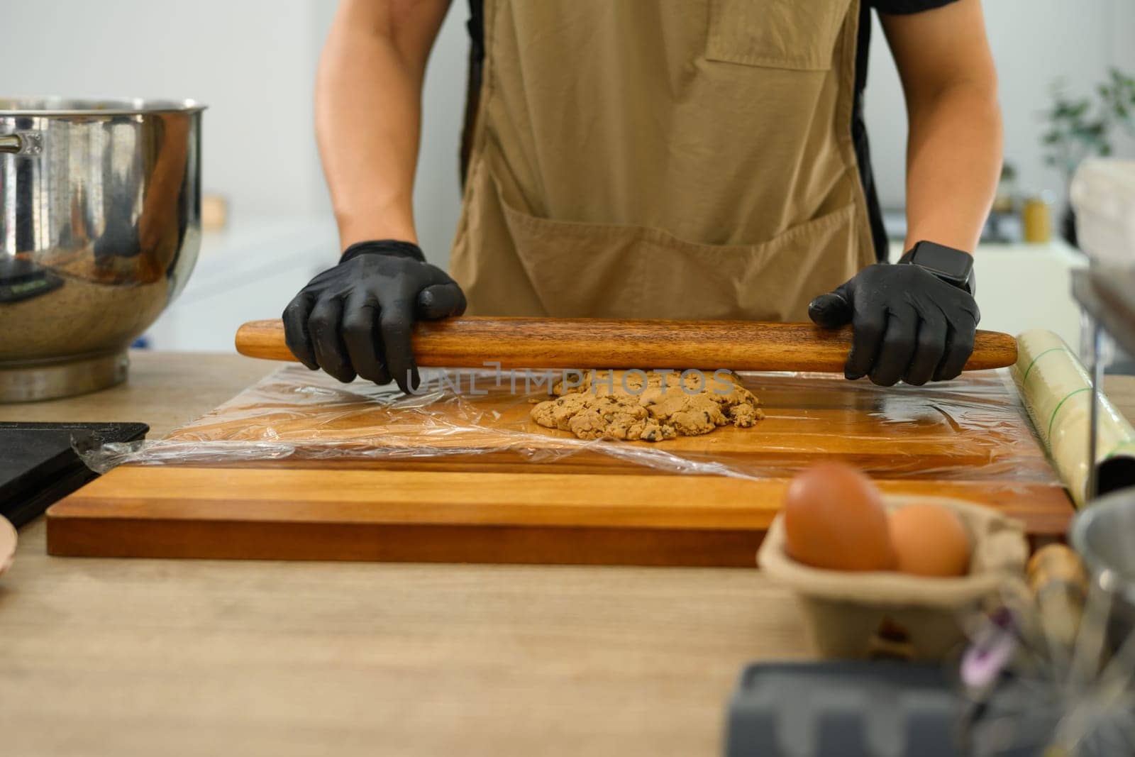 Close up of a baker flattening chocolate chip cookie dough with a wooden rolling pin.