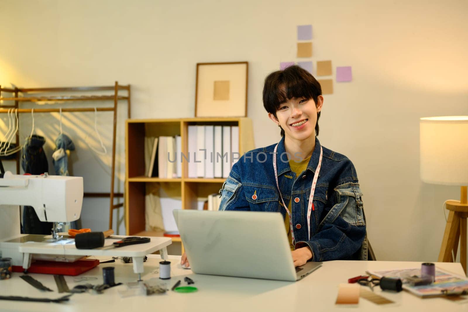 Smiling fashion designer working on a laptop in a studio.