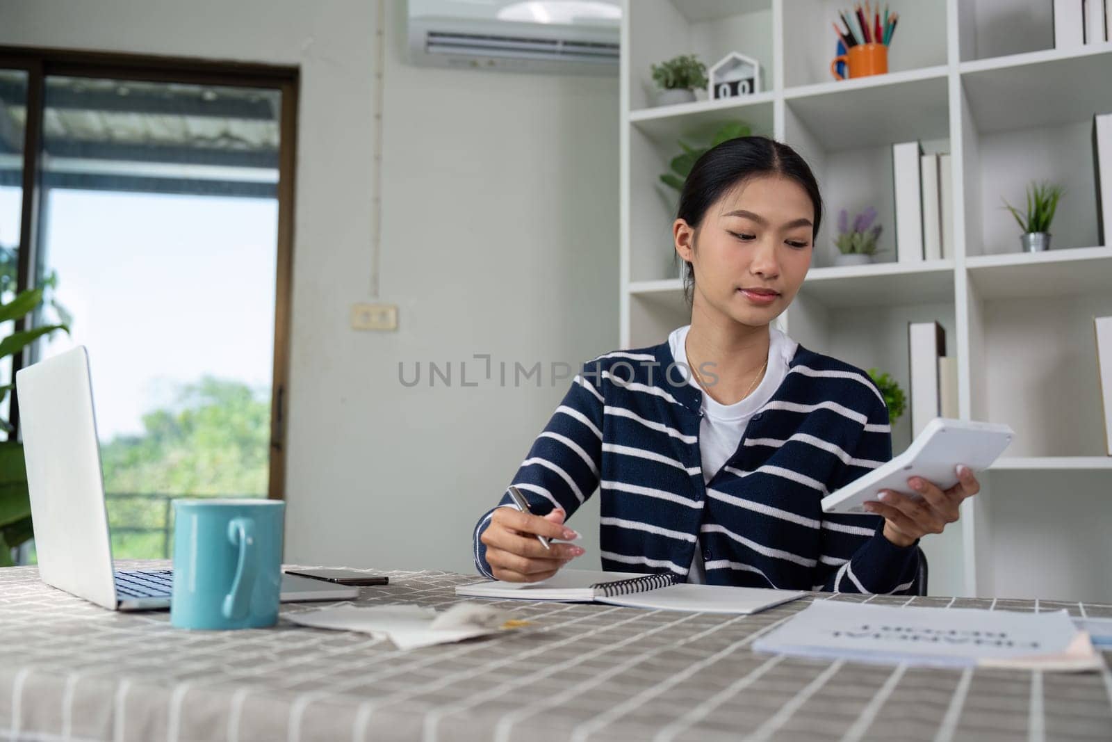 A young woman calculates her finances using a calculator, notebook, and bills, emphasizing personal financial management.