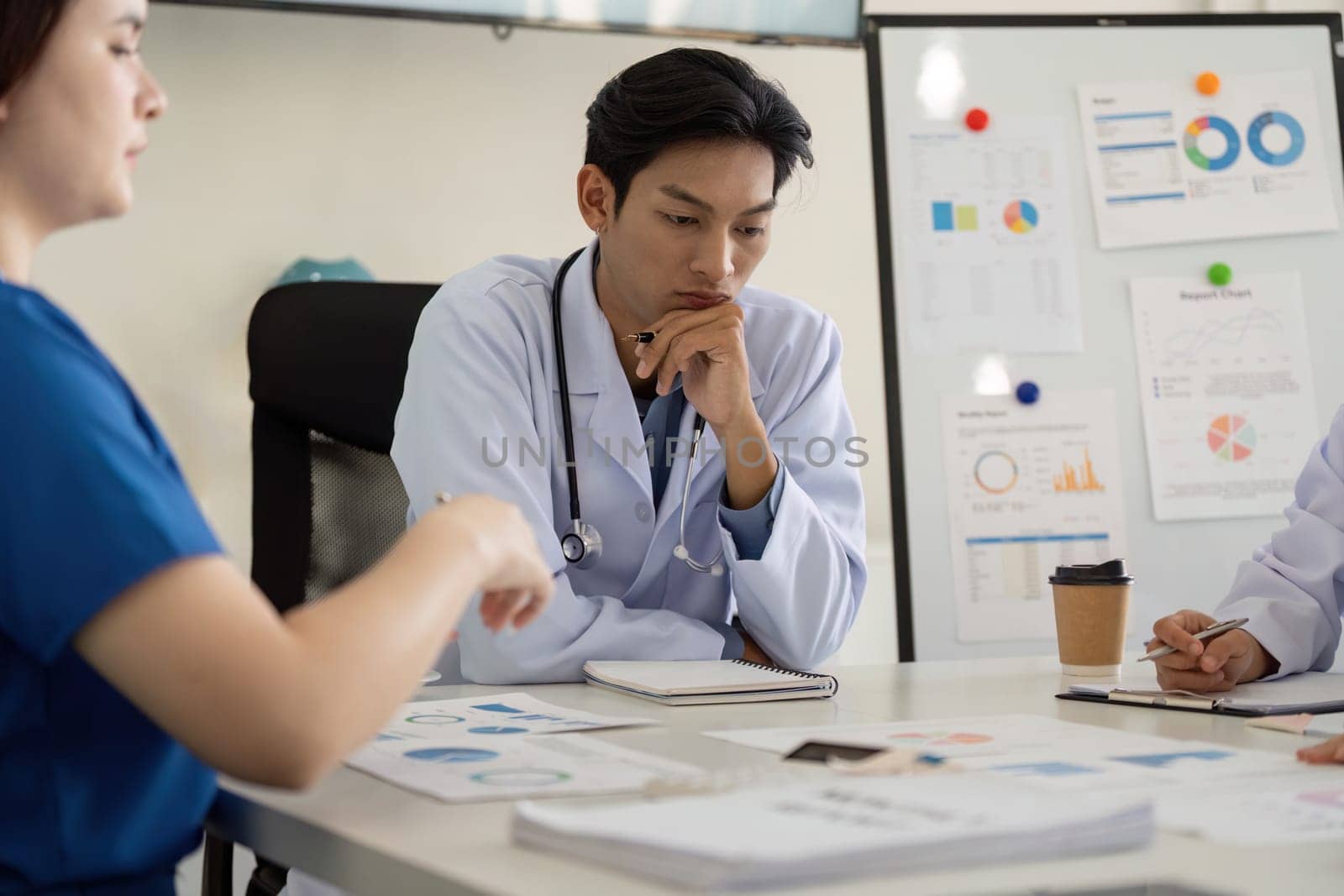 A diverse group of healthcare professionals, including a physician and nurse, analyze charts and discuss strategies during a meeting.