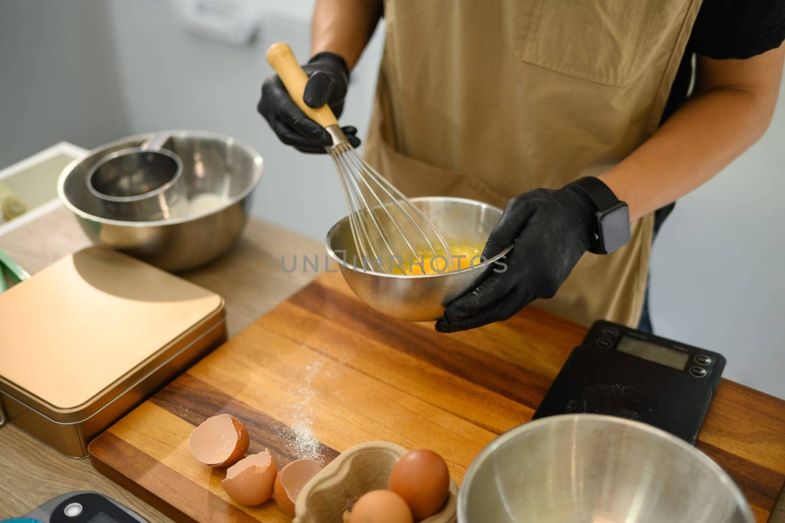 Cropped shot of baker whisking eggs in a stainless steel bowl, preparing cookie dough.
