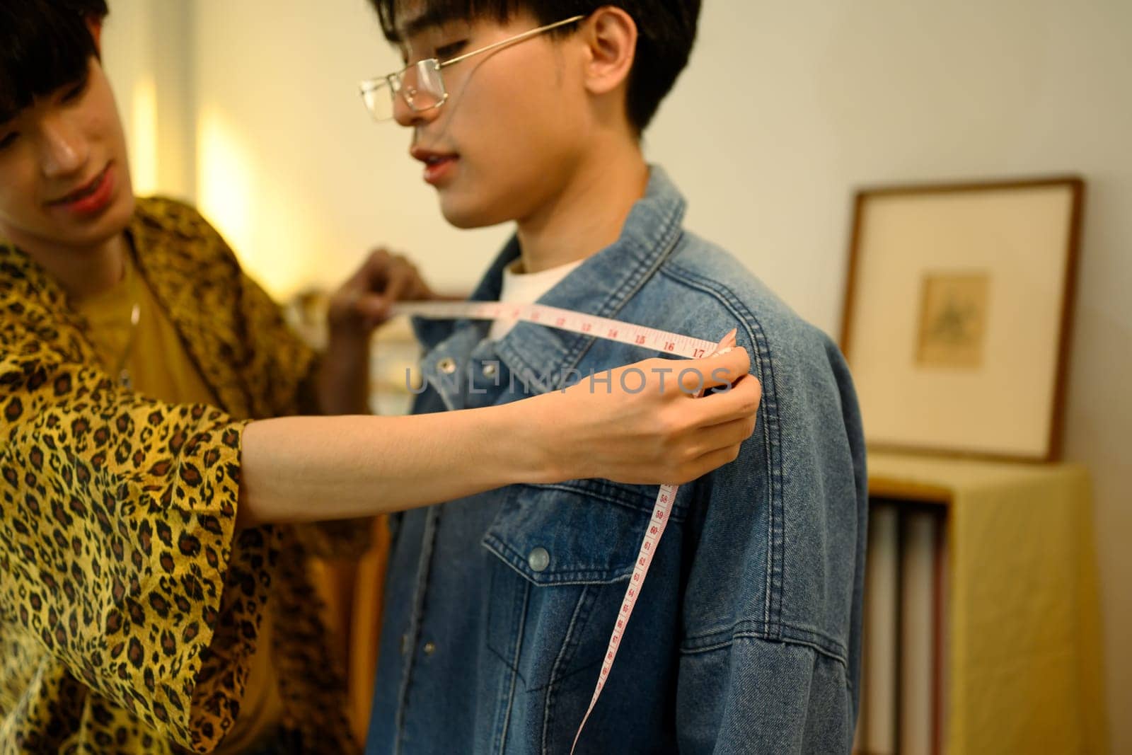 Tailor measuring a client shoulder with measuring tape for custom clothing.