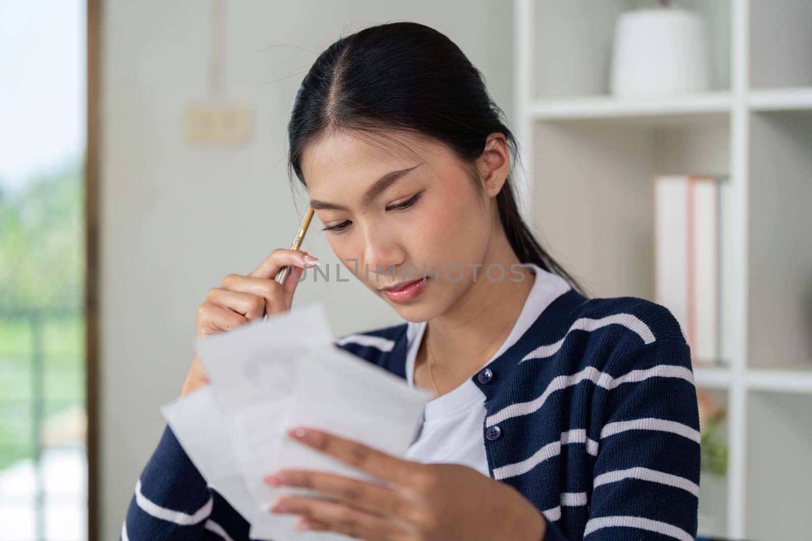 A young woman thoughtfully reviews her financial documents and bills at home, focusing on budgeting and financial literacy.