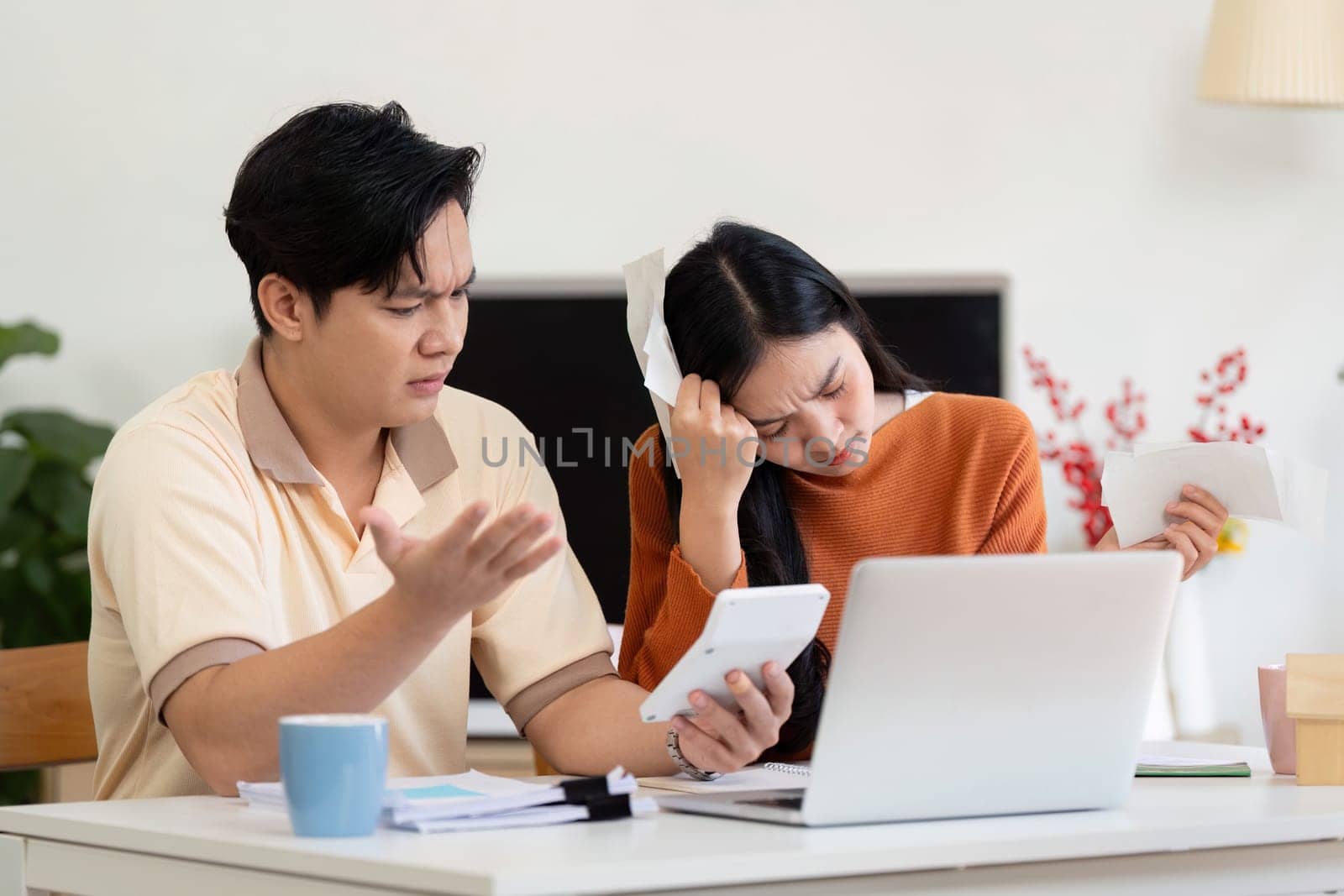 A couple is calculating their income and bills at home, showing concern and teamwork in financial management.