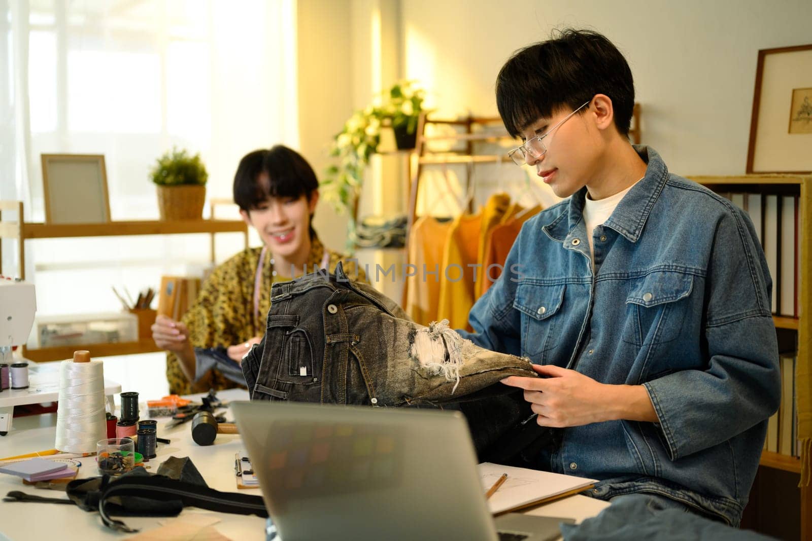 Two fashion designers collaborating on custom denim project in a stylish studio.