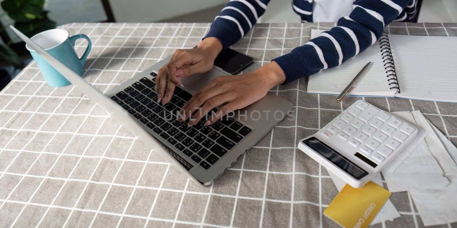 A young woman reviews financial documents while using a calculator and laptop, illustrating the importance of budgeting and financial planning.