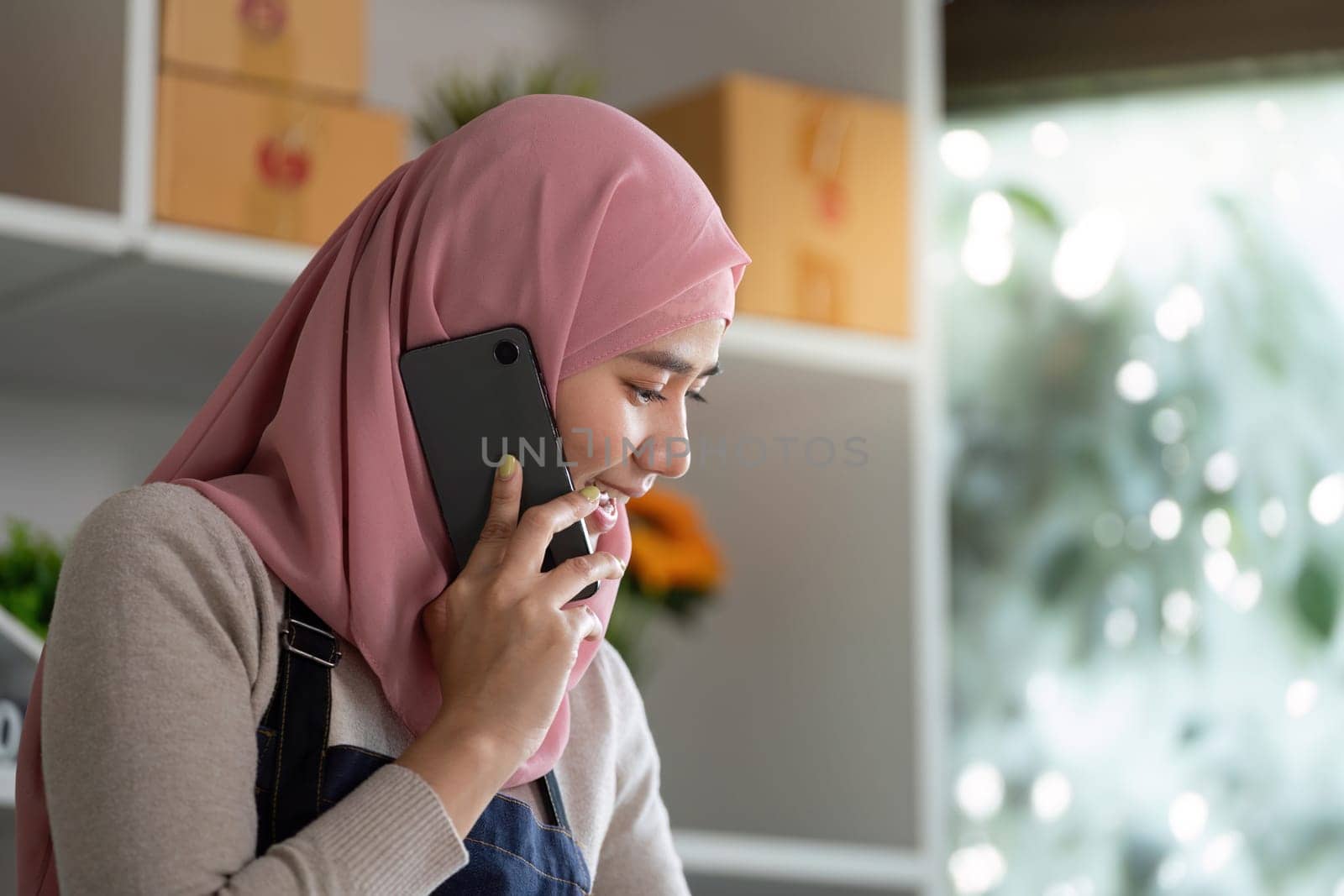 A Muslim woman in a hijab speaks on the phone, effectively managing her online business operations in a contemporary workspace.