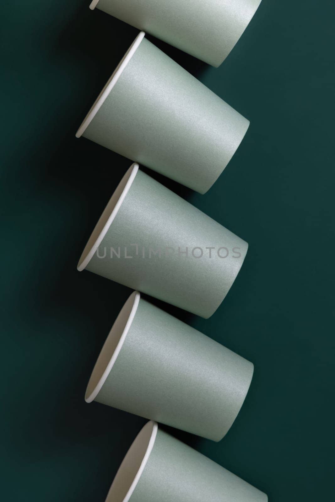 Disposable light green paper cups on a dark green background top view, mockup with advertising copy space. Empty cardboard coffee cups flat lay. No plastic and sustainable lifestyle concept