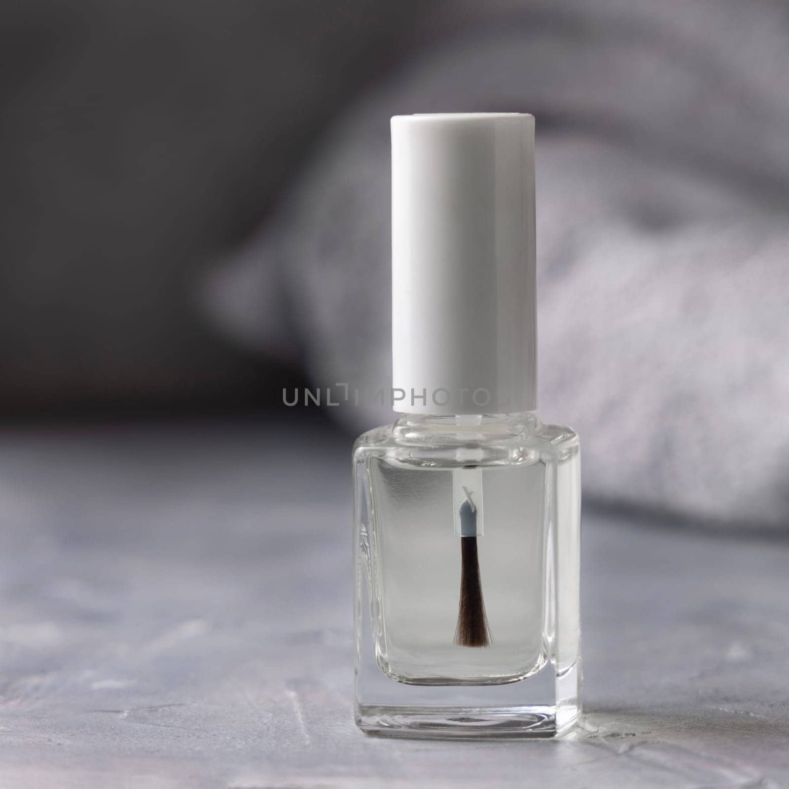 Clear glass refillable bottle with white blank brush cap near grey bath towel on grey close up, cosmetics mockup. Natural skincare nail product, minimal aesthetic