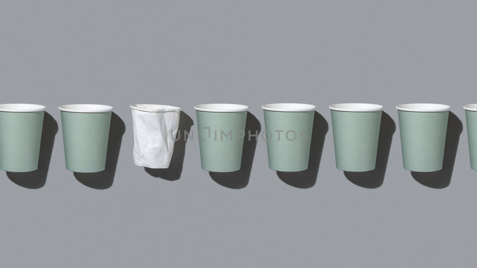 Disposable new light green paper cups and crumpled used white one in a line on gray top view, hard shadow, mockup with copy space. Empty cardboard coffee cups flat lay. Consumerism concept