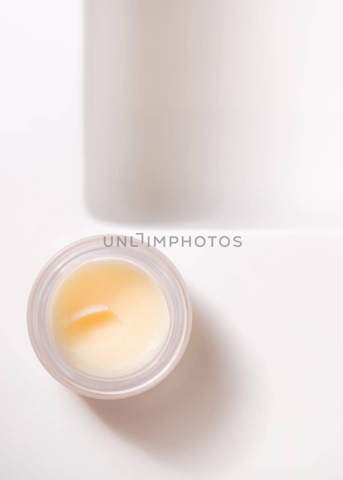 Opened lip balm jar with blank lid on white washbasin top view, cosmetic packaging mockup, copy space. Lipcare beauty product for everyday personal care or spa procedures