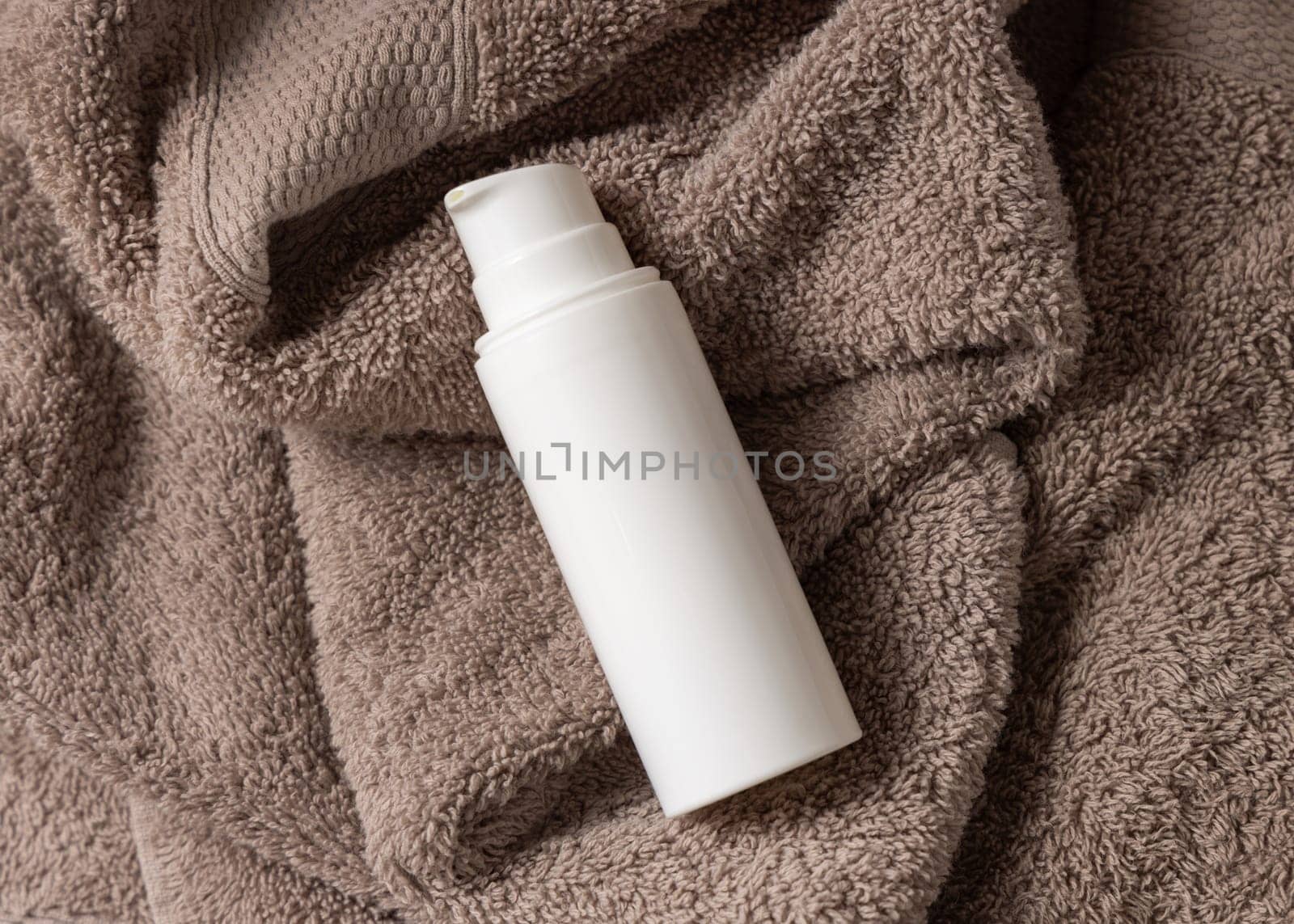White blank one pump cream bottle on brown towel in bathroom top view, brand packaging mockup. Natural herbal cosmetic product - cream, lotion or foam for daily facecare, copy space