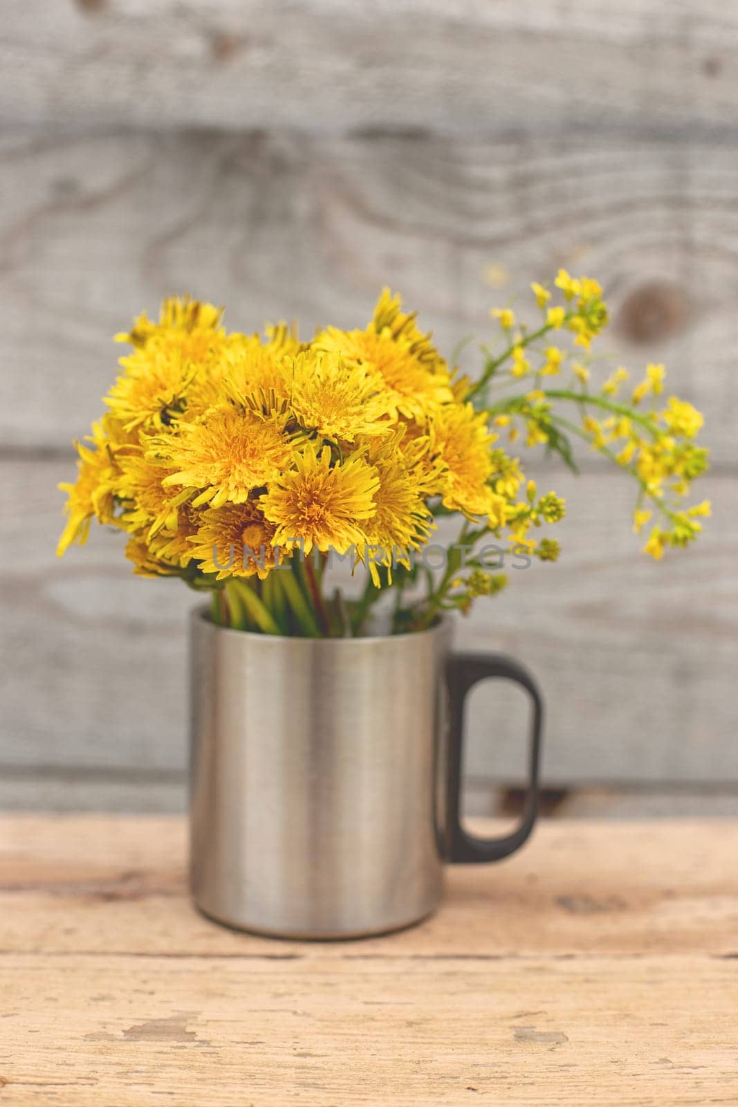 Dandelion bouquet in a metal mug. Vertical. Wood background