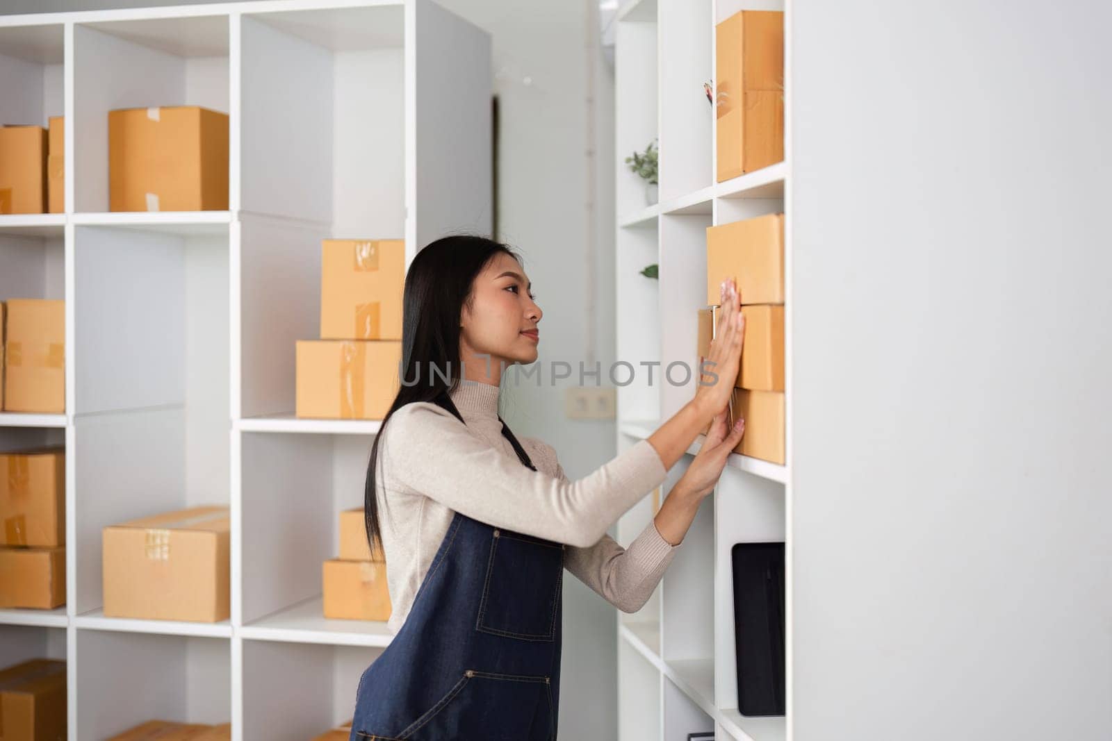 A young woman organizes boxes in a modern office space, reflecting her entrepreneurial spirit and commitment to her business.
