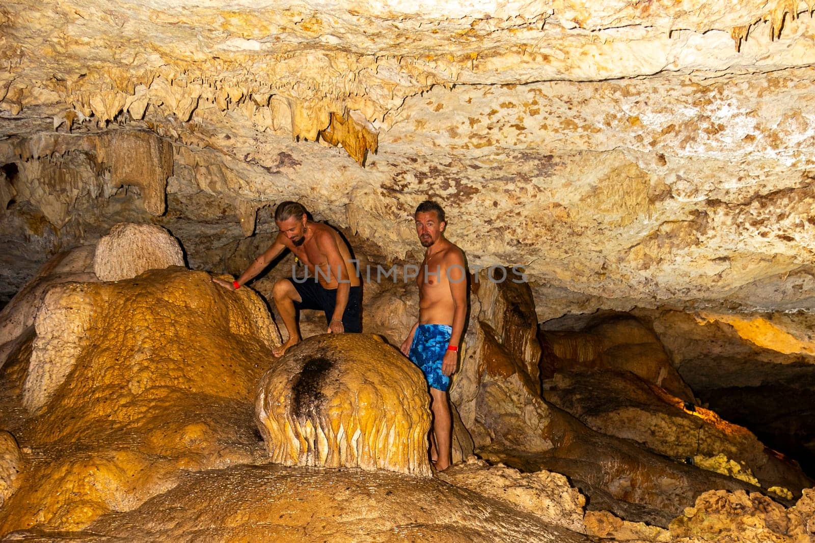 Mean male tourists friends are posing and climbing in the turquoise green blue water and rocks in cenote Yaxmulito in Tulum Quintana Roo Mexico.