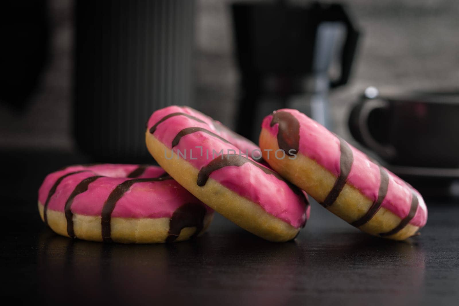 Sweet pink donut with chocolate strips on a black table.