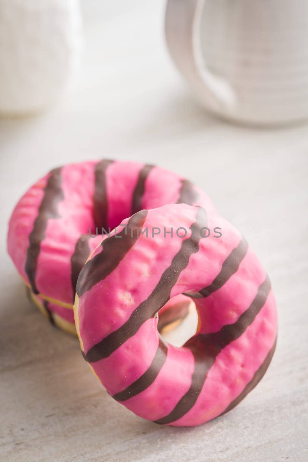 Sweet pink donut with chocolate strips on a kitchen table.