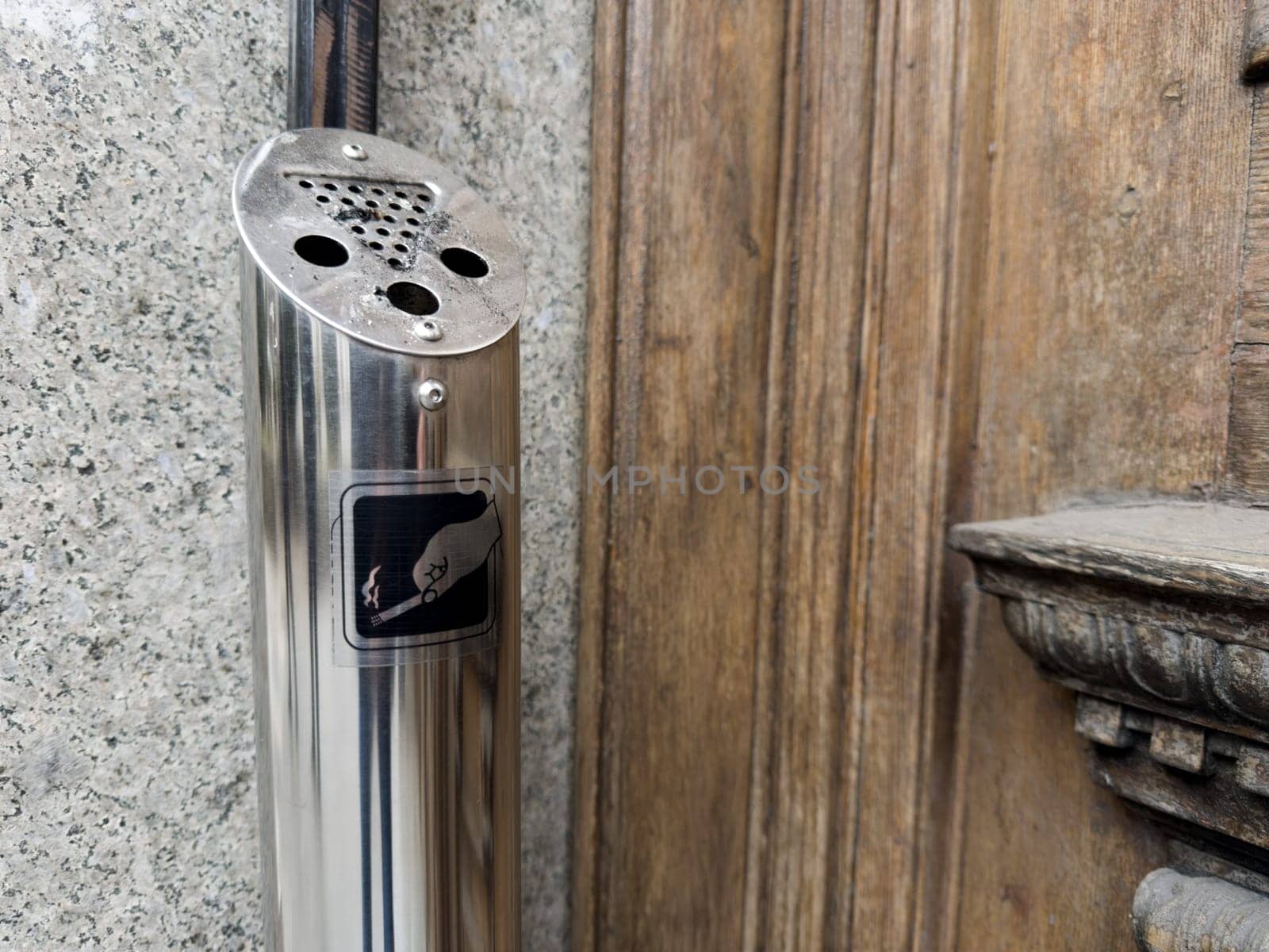 Steel outdoor ashtray for heavy smokers. Convenient ashtray is located at entrance to building. Trash of cigarette butts after smoking on street. Cigarette icon on metal ashtray in smoking area