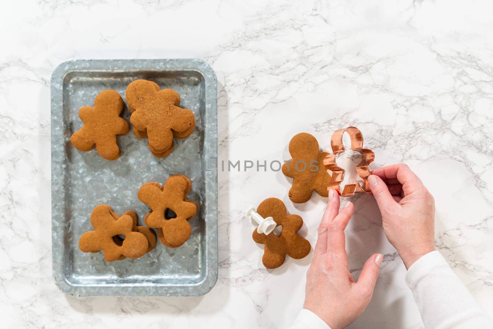 Flat lay. Gingerbread cookies, including a gingerbread man with a heart-shaped cutout, rest on a rustic metal tray against a marble countertop.