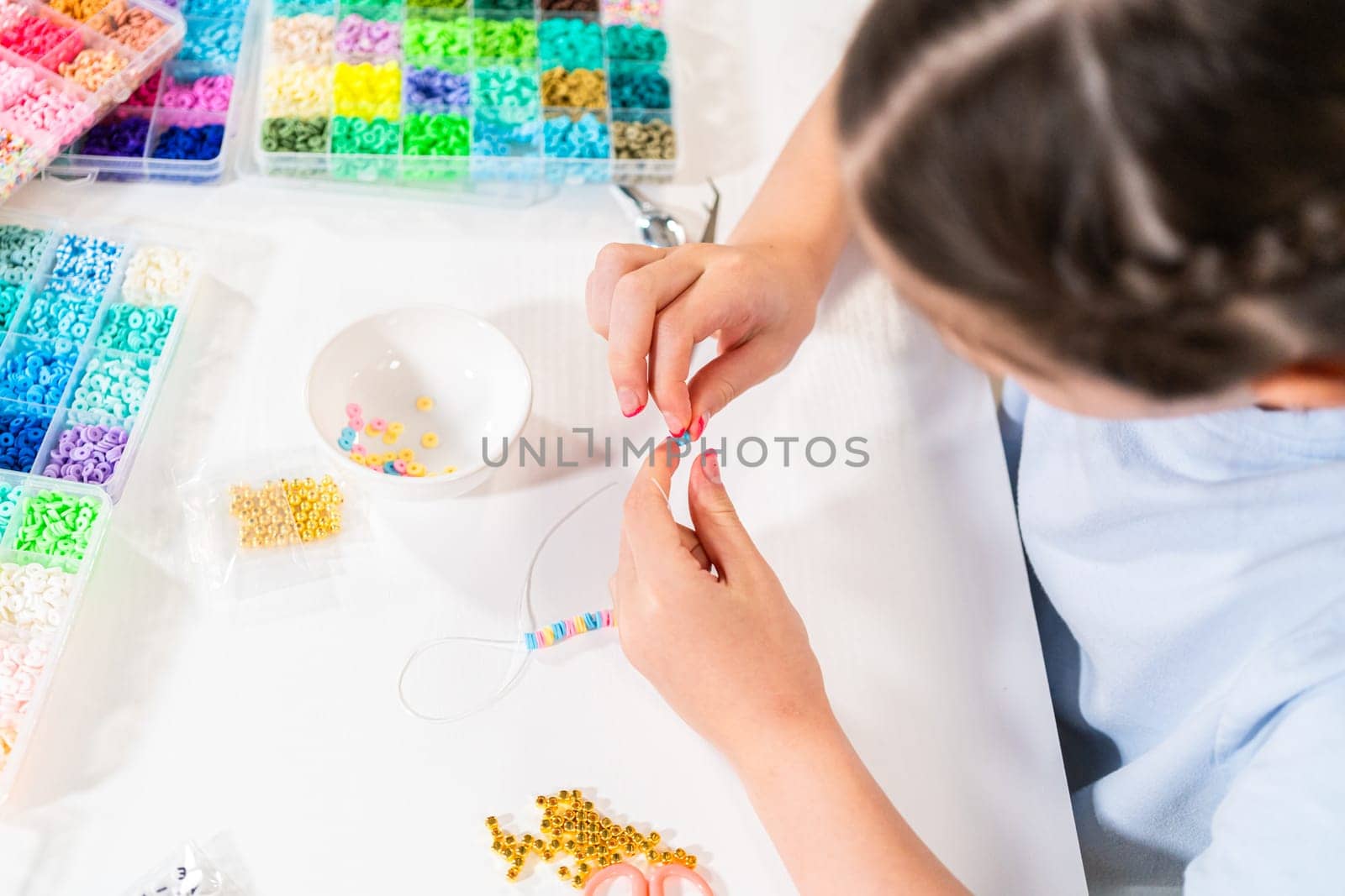 Little girl enjoys crafting colorful bracelets with vibrant clay beads set.