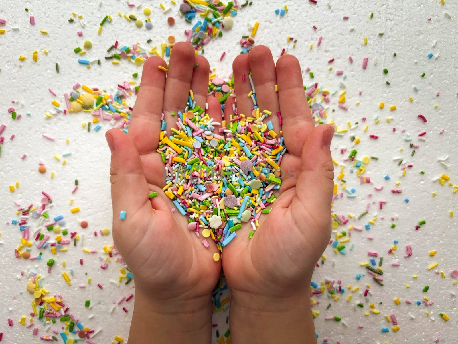 Close-up of child's hands playing with colorful sprinkles on table.