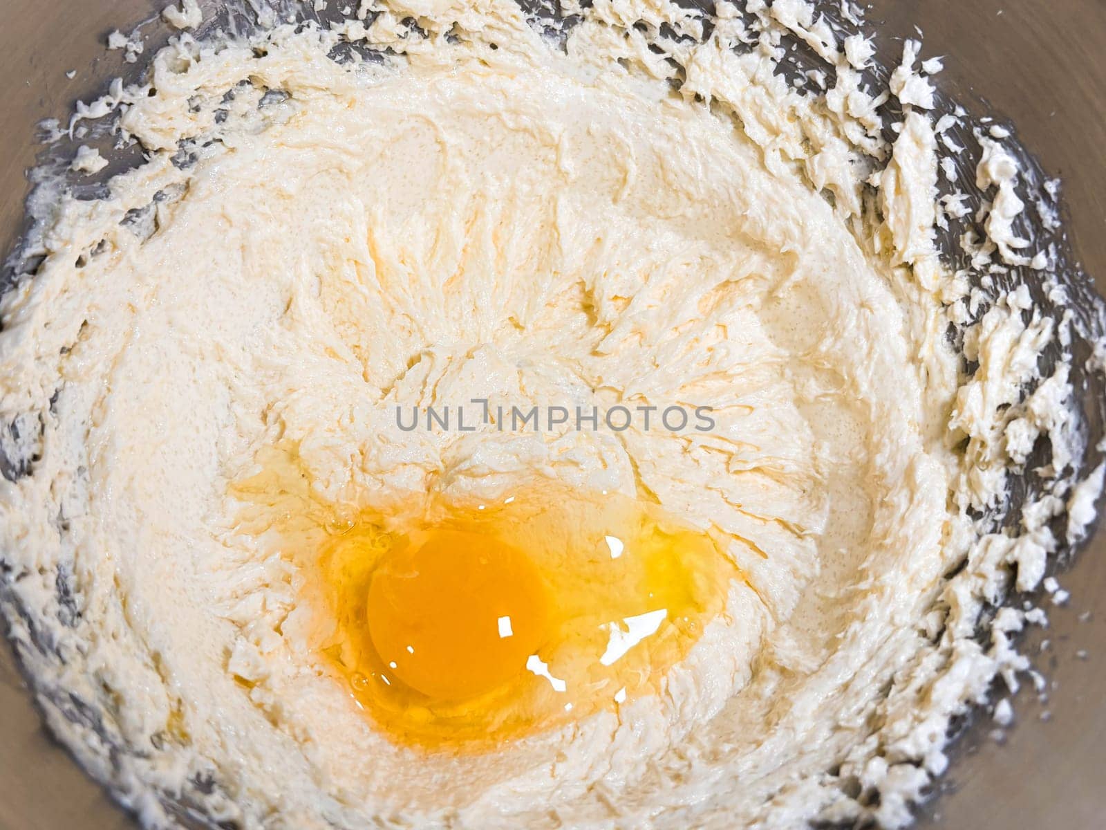 Beating butter, sugar and eggs in a grey metal bowl. The process of making cake and cookies by mixing butter, eggs and sugar. Close-up of an egg in cream.