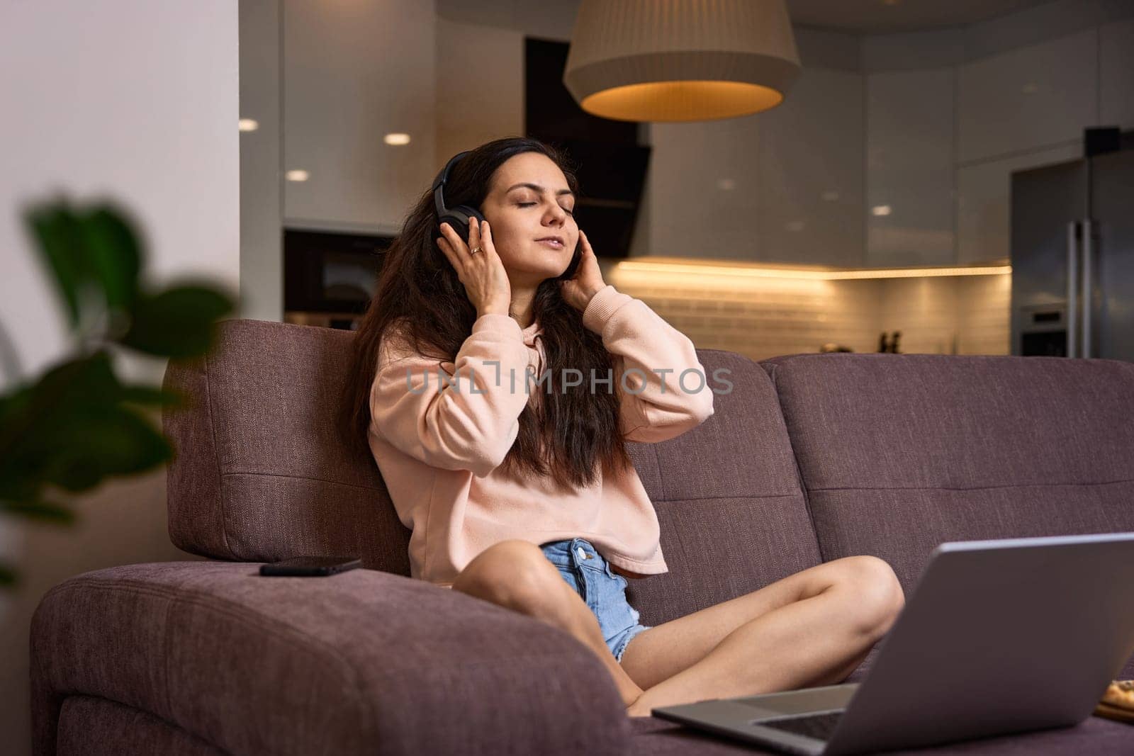 happy Caucasian woman listening to music with headphones and using laptop on couch at home