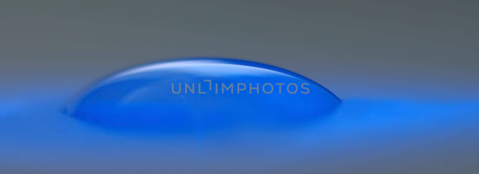 A drop of water on a sheet of paper is just sucking in and is brightened by a blue light-emitting diode.