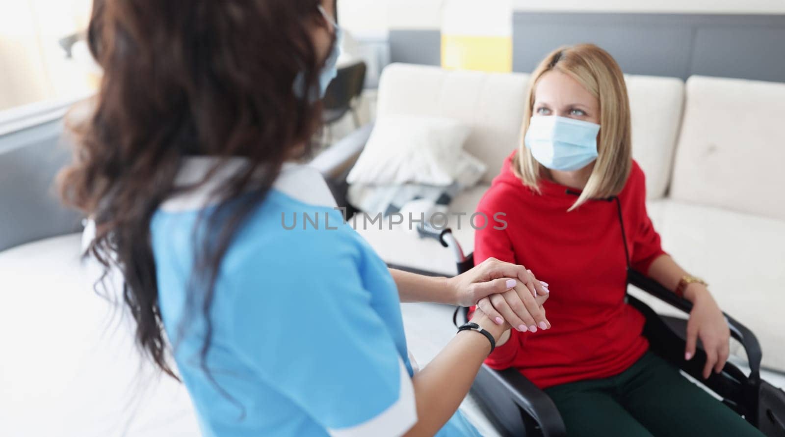 Woman in wheelchair in protective medical mask gives hands to doctor. Coronavirus and disability concept