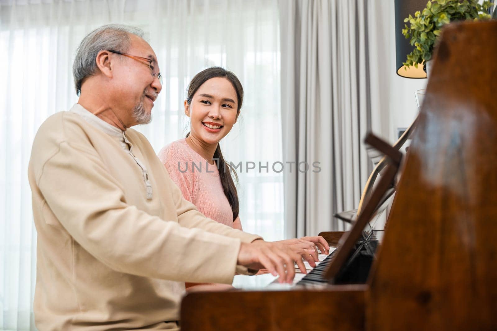 Family. Young woman teaching piano for senior man teaching, happy daughter and elderly father with eyeglasses relaxation playing piano together in living room at home, lifestyle life after retirement