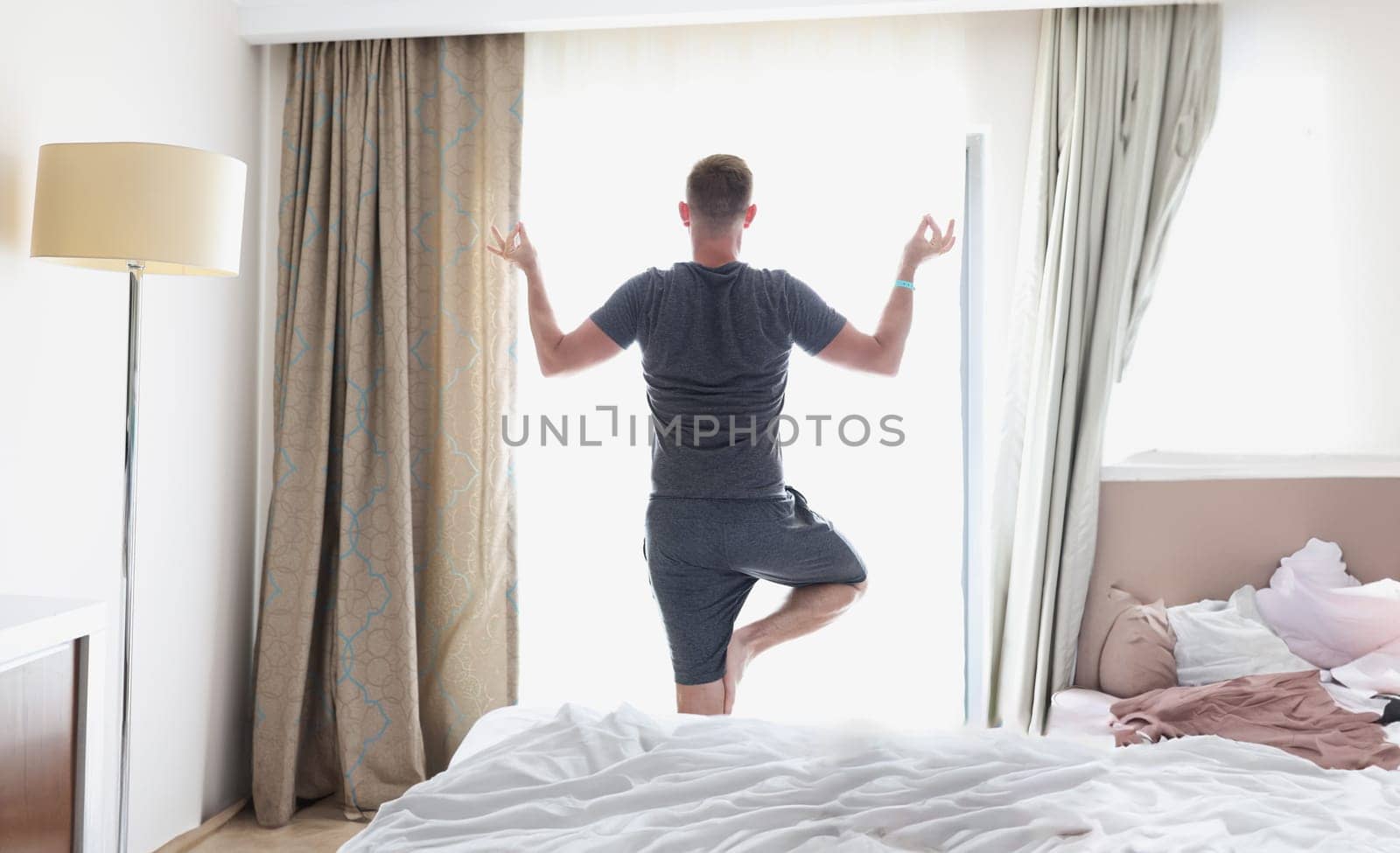 Man stands in lotus position by window. Morning exercise and relaxation concept