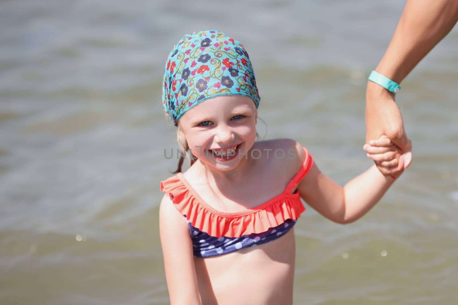Smiling little girl in swimsuit and a scarf at sea. Rules for finding children in the sun concept