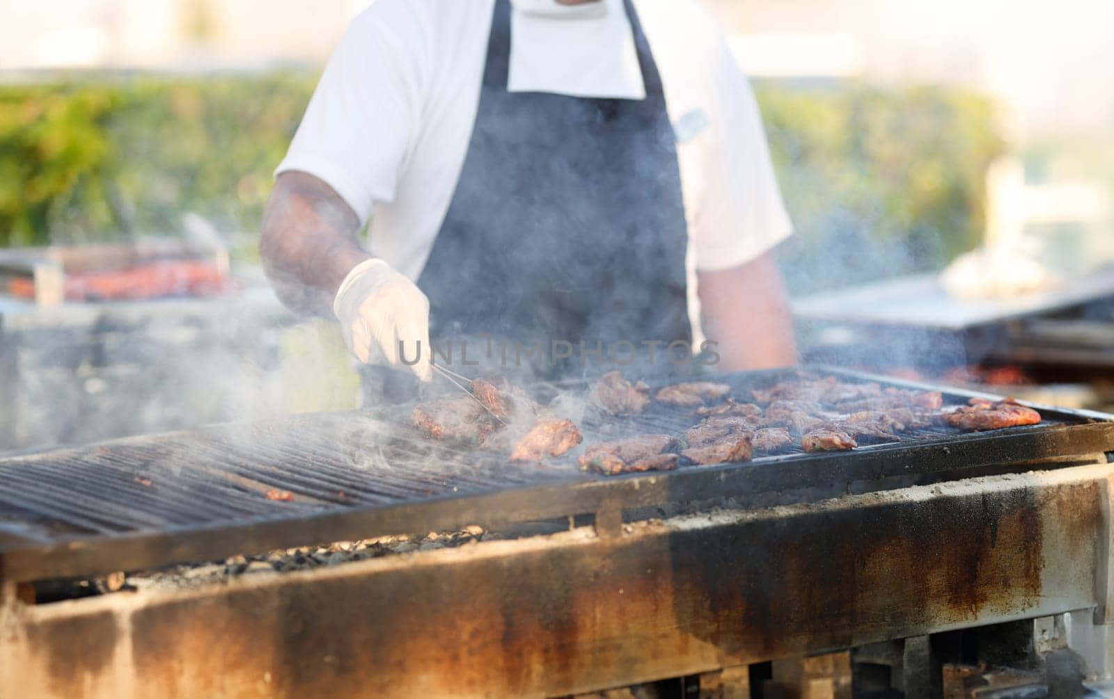 Gloved chef turns meat on grill with tongs. Grilled meat recipes on the grill concept