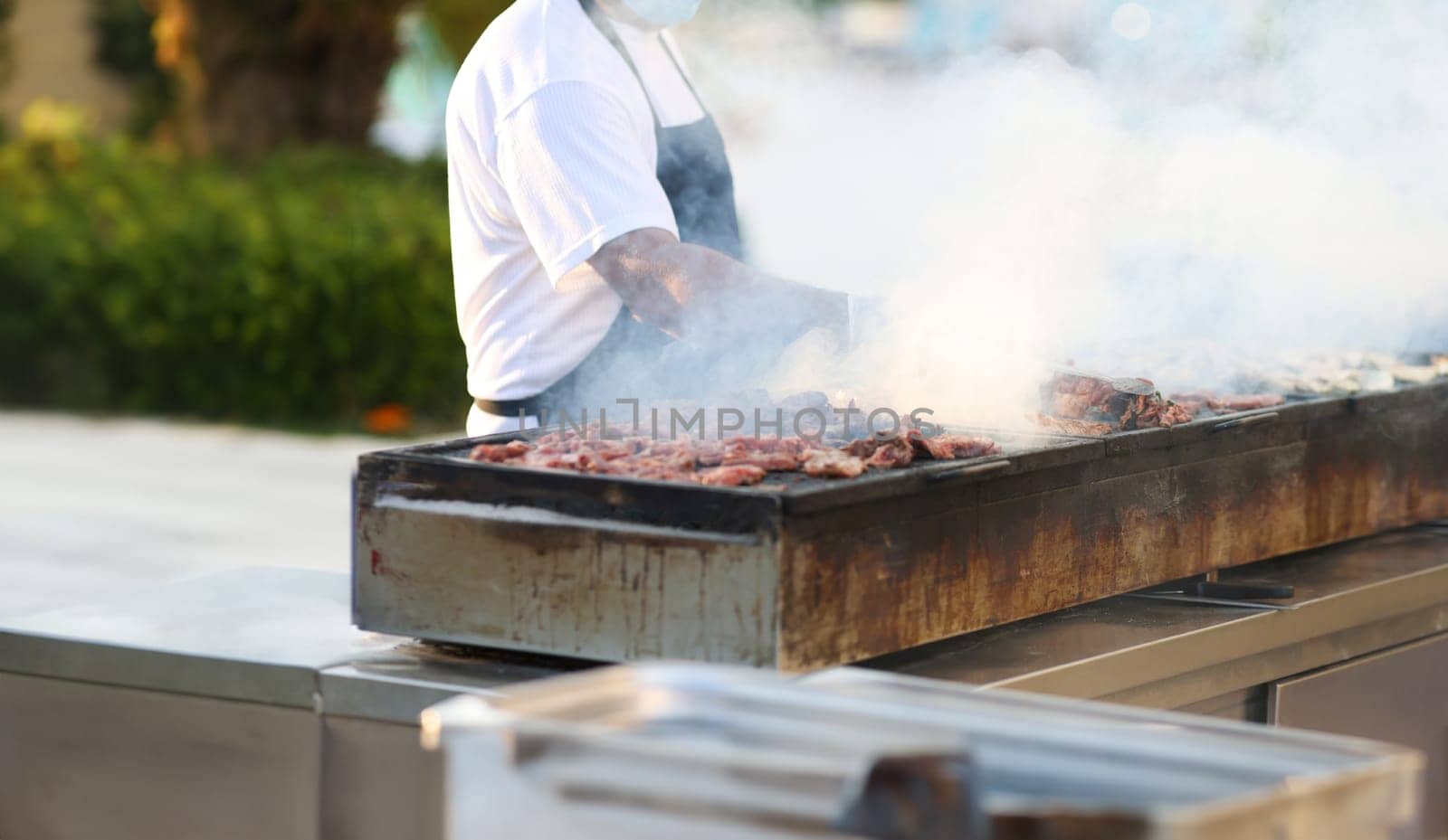 Cook prepares meat on coals in the open air. Offsite themed catering concept