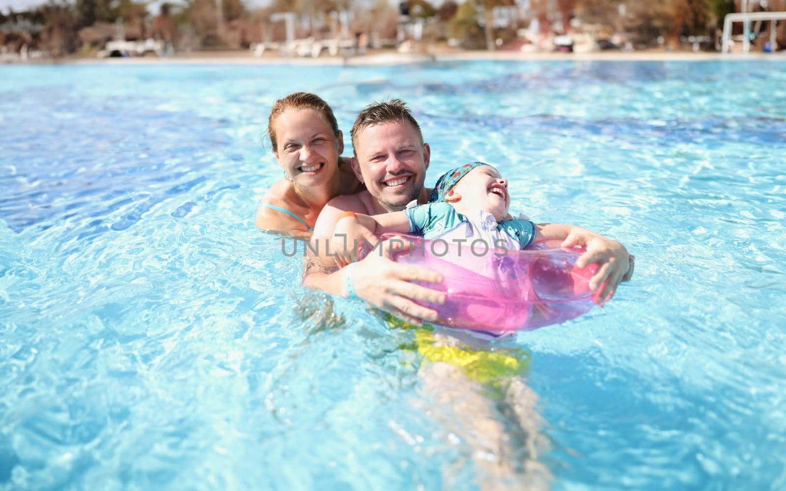 Family mom dad and daughter laugh and swim in pool. Travel and vacation with children concept