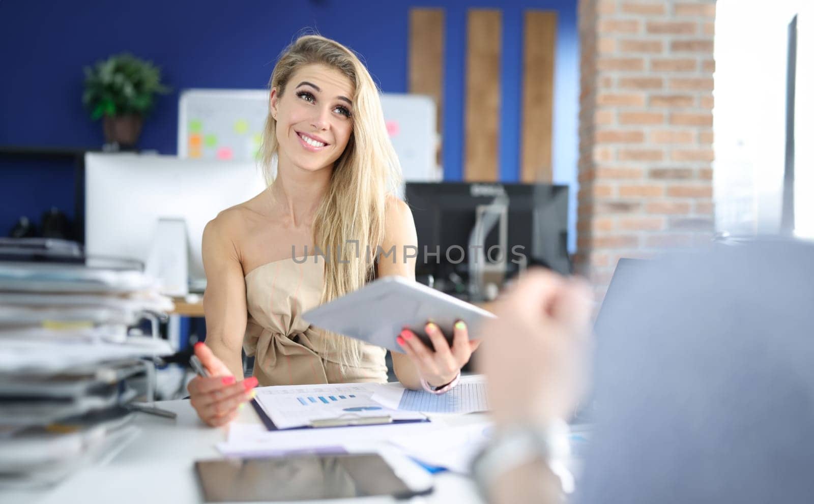 Smiling businesswoman at her working table in office holds tablet and studies business indicators. Profitable cooperation and interaction concept