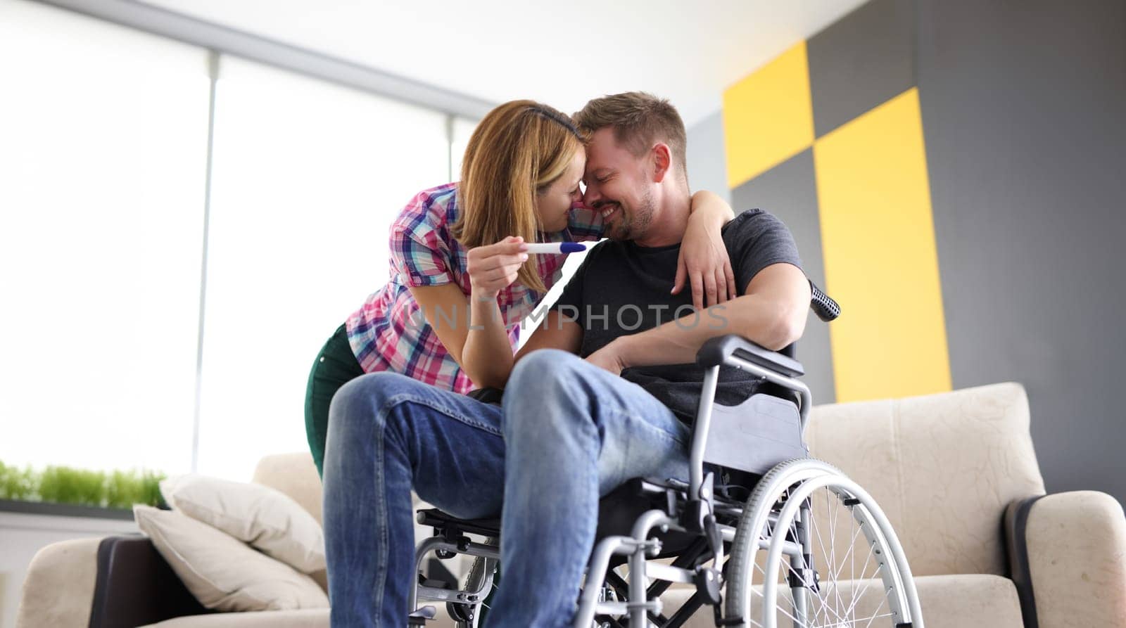 Joyful woman and man in wheelchair with pregnancy test. First emotions of future parents concept