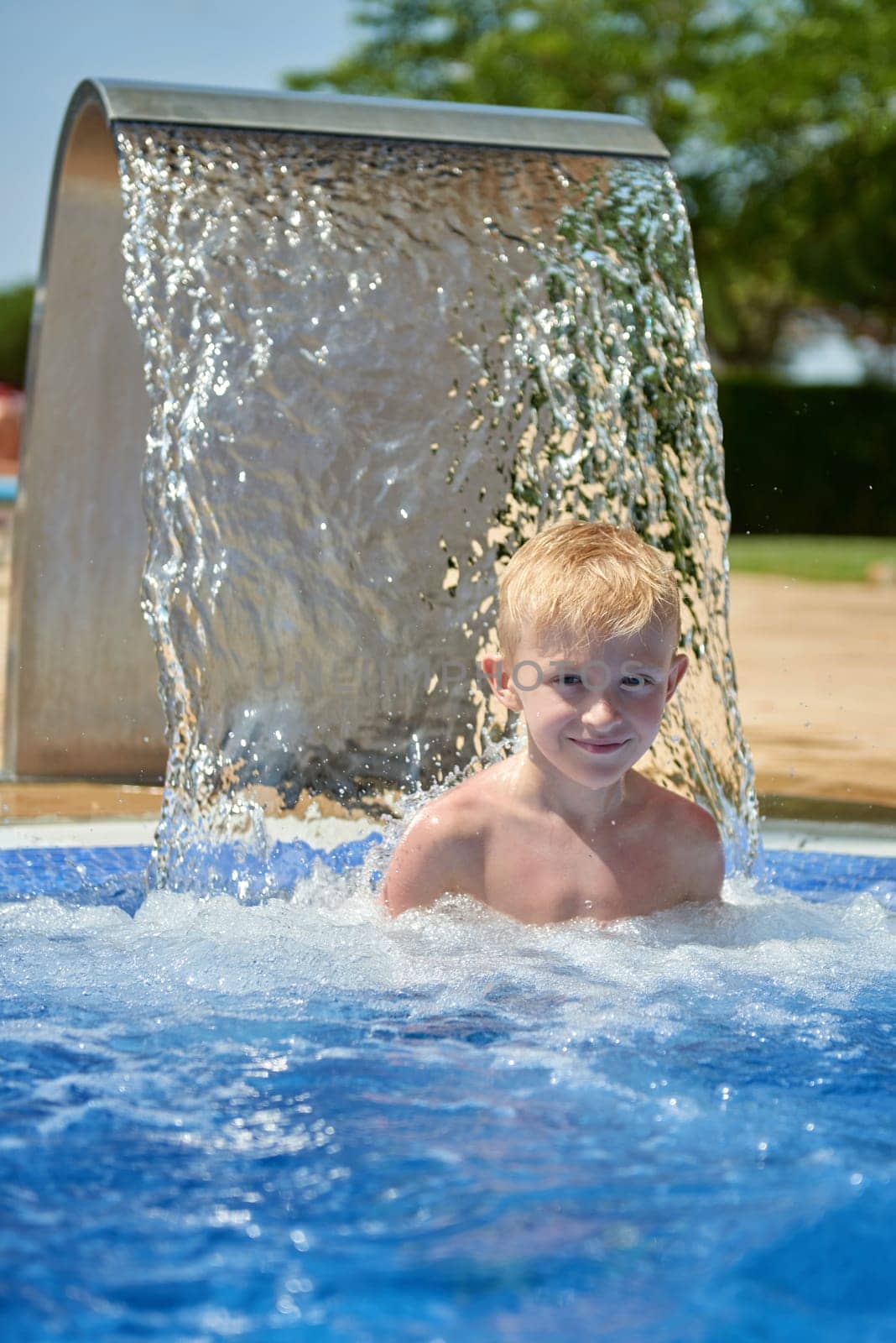 Young boy kid child eight years old splashing in swimming pool having fun leisure activity. Boy happy swimming in a pool. Activities on the pool, children swimming and playing in water, happiness and summertime