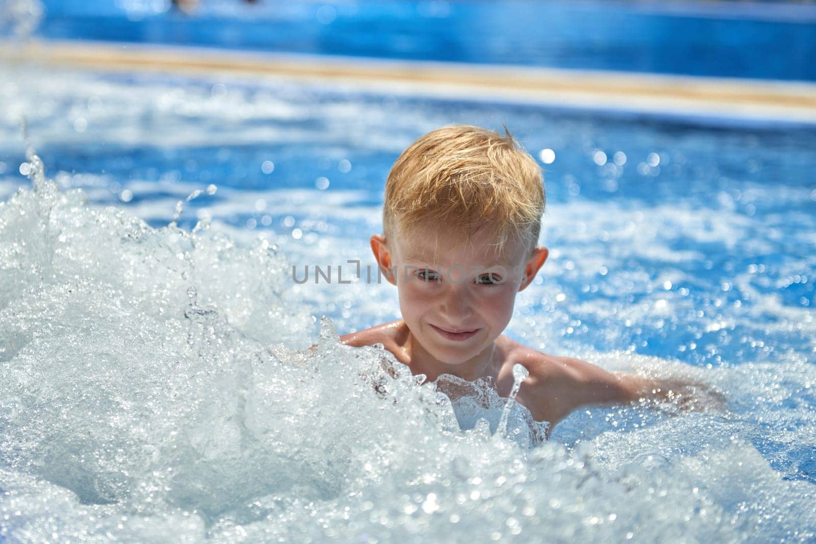 Young boy kid child eight years old splashing in swimming pool having fun leisure activity. Boy happy swimming in a pool. Activities on the pool, children swimming and playing in water, happiness and summertime