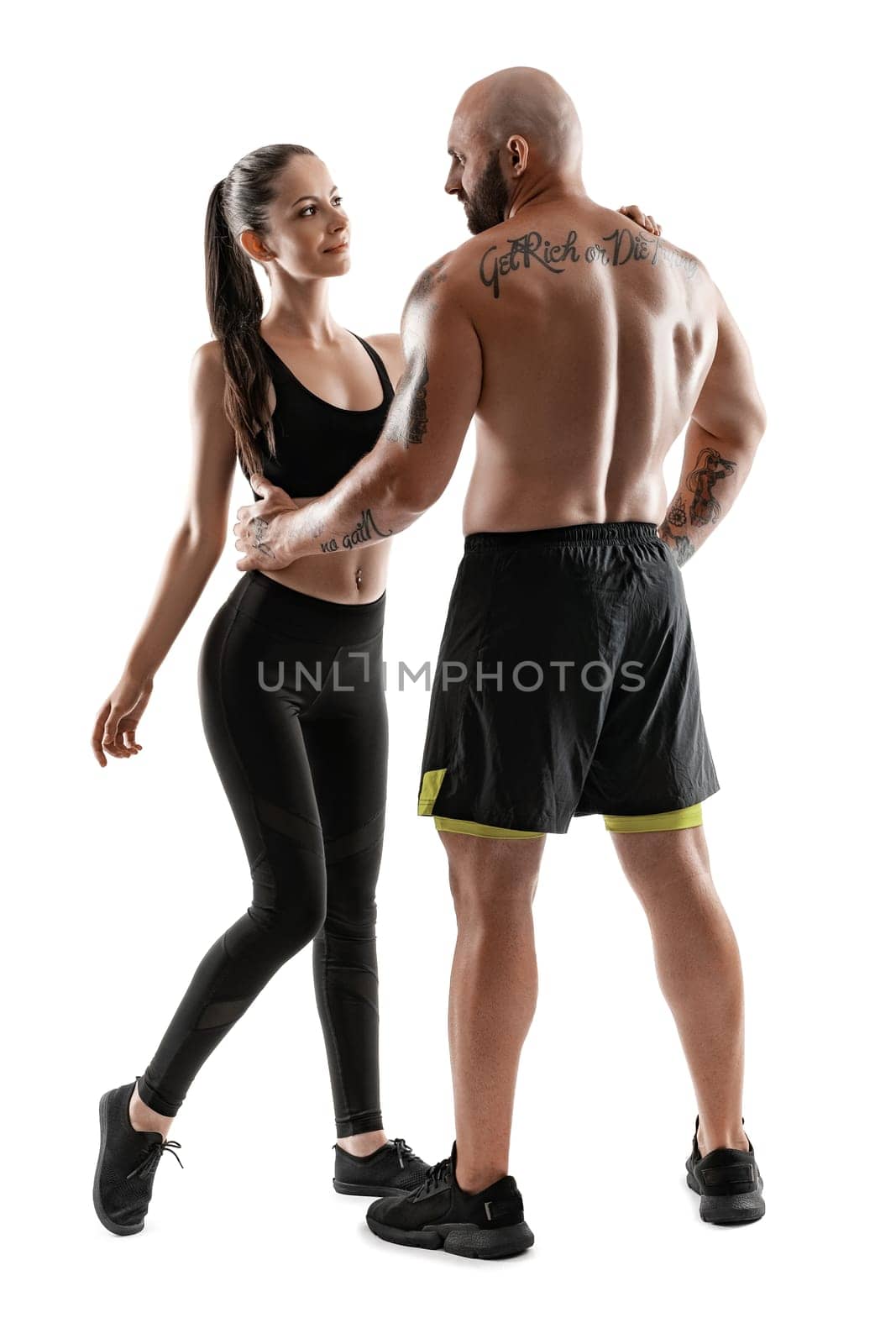 Athletic man in black shorts and sneakers with brunette woman in leggings and top posing isolated on white background. Fitness couple, gym concept. by nazarovsergey