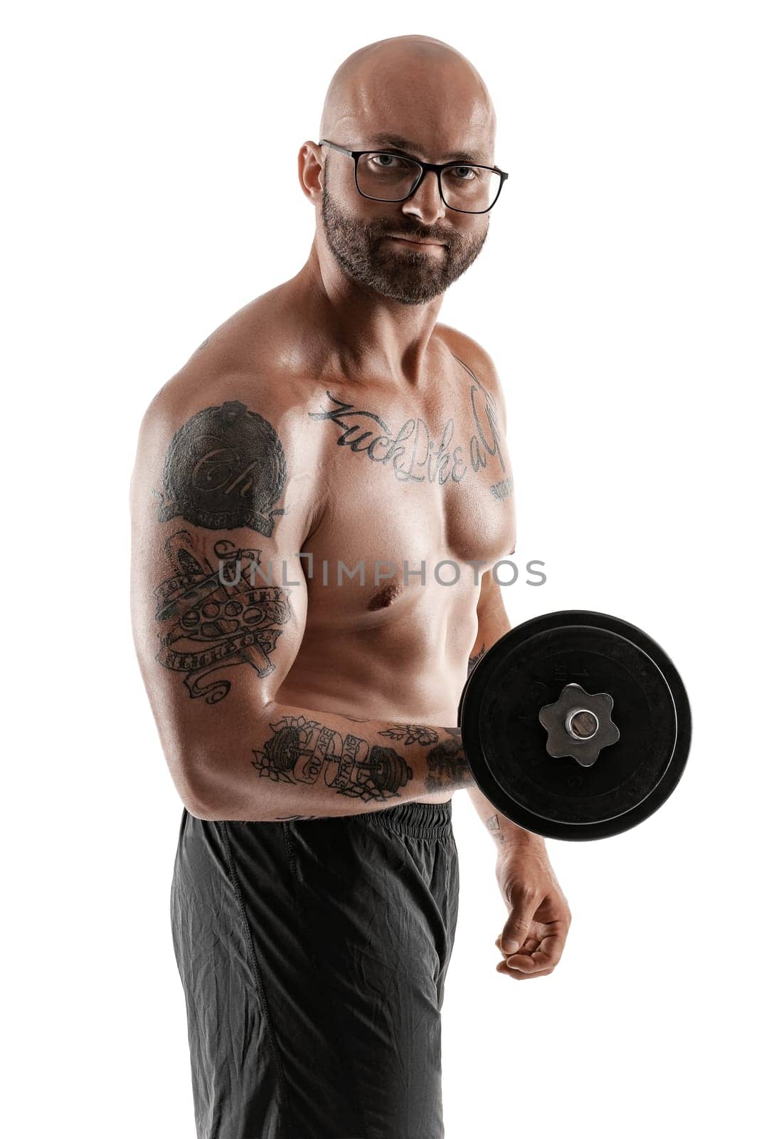 Handsome bald, bearded, tattooed guy in glasses, black shorts is posing holding a dumbbell in his hand isolated on white background and looking at the camera. Chic muscular body, fitness, gym, healthy lifestyle concept. Close-up portrait.