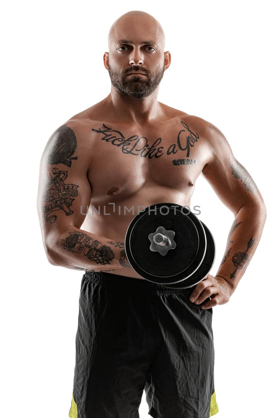 Handsome bald, bearded, tattooed person in black shorts is posing holding a dumbbell in his hand and looking at the camera, isolated on white background . Chic muscular body, fitness, gym, healthy lifestyle concept. Close-up portrait.