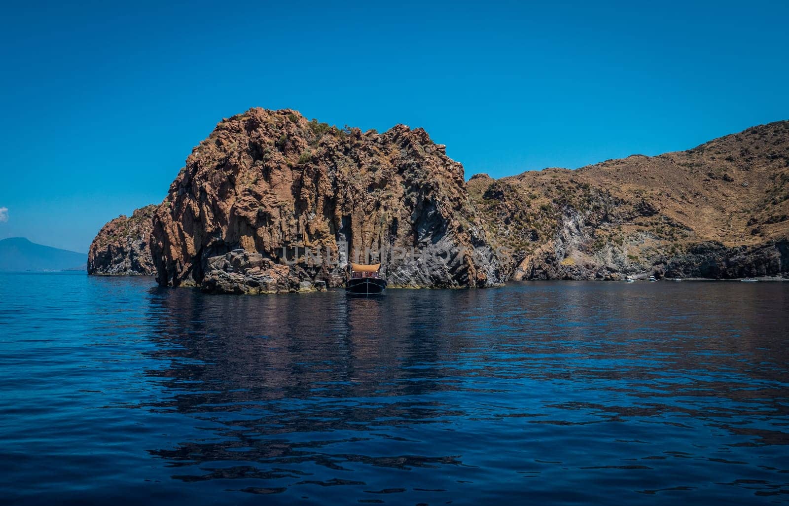 A small boat in the middle of a body of water. Photo of a serene boat floating in the crystal clear waters of Sicily's Eolie Islands