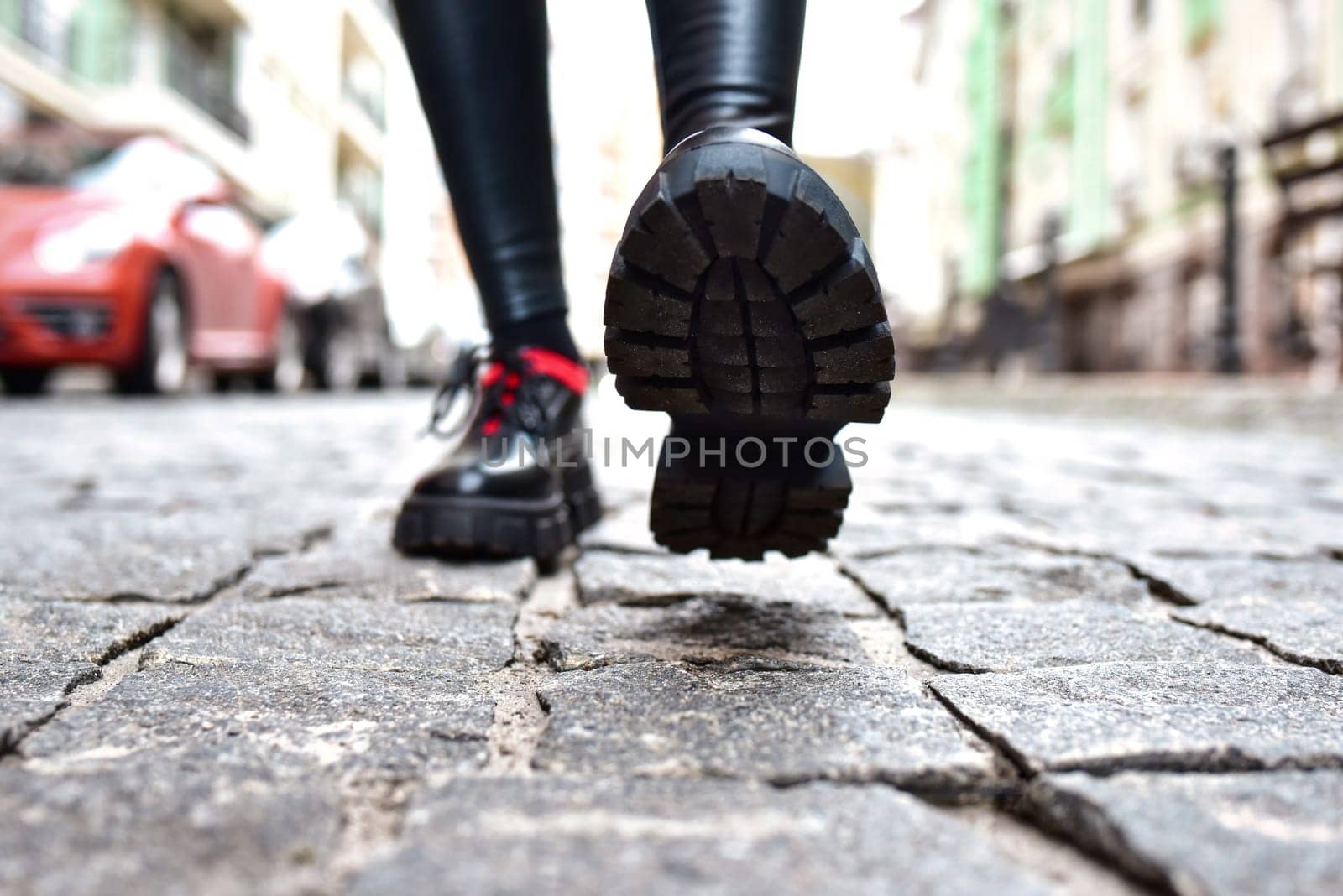 Female legs view in black leggings and black shoes walking down the street in the city. by Nickstock