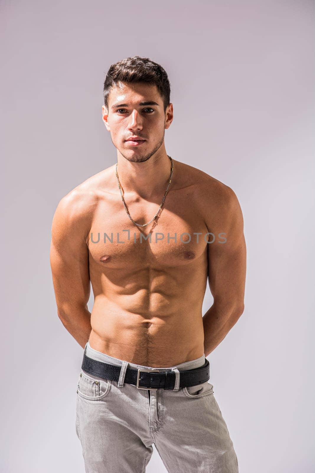 A shirtless handsome young man posing for a picture showing muscular torso, looking at camera, wearing grey jeans