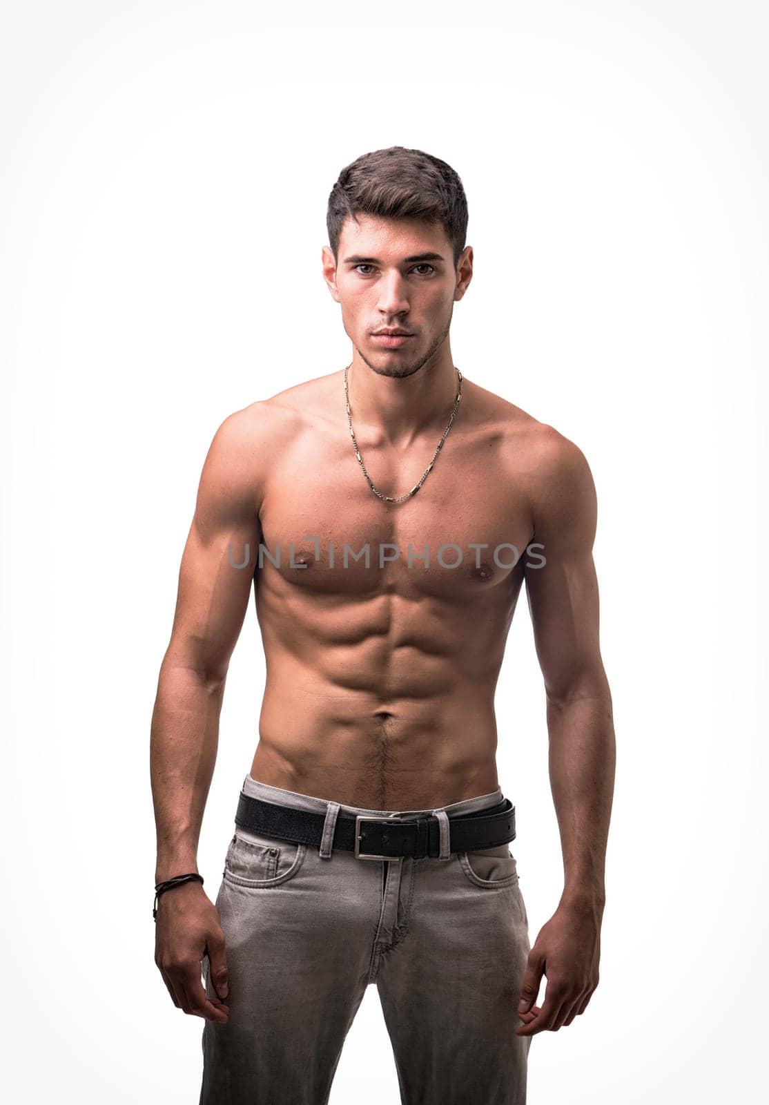 A shirtless handsome young man posing for a picture showing muscular torso, looking at camera, wearing grey jeans