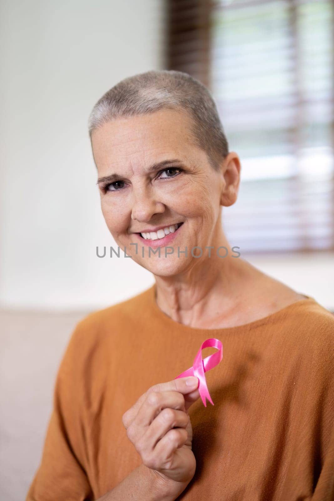 Portrait of confident smiling elderly senior woman with pink ribbon at her home. Health care, support, prevention. Breast cancer awareness month concept by nateemee