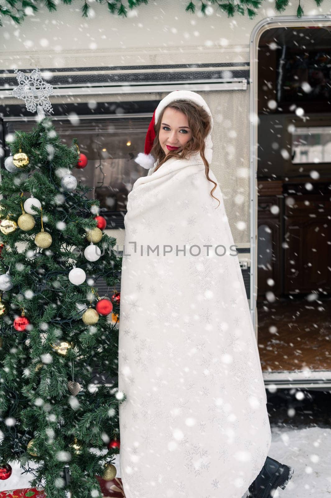 Young woman in santa costume decorates the Christmas tree at winter campsite getting ready for the new year. New year celebration concept