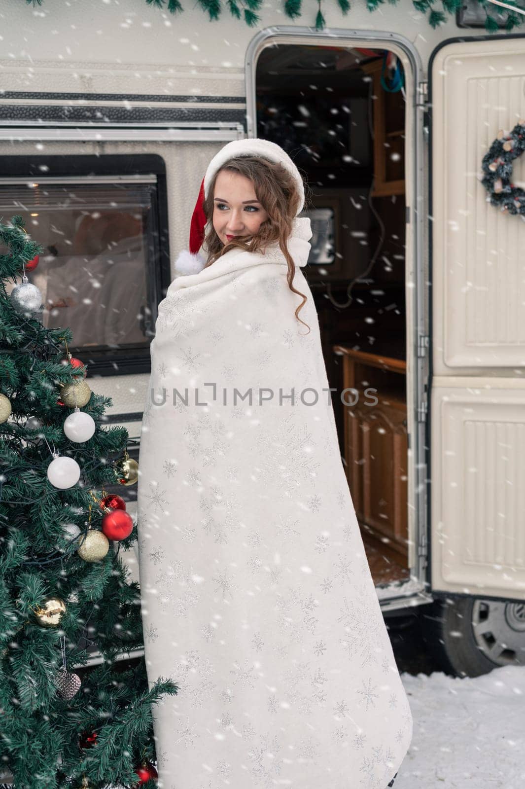 Young woman in santa costume decorates the Christmas tree at winter campsite getting ready for the new year. New year celebration concept